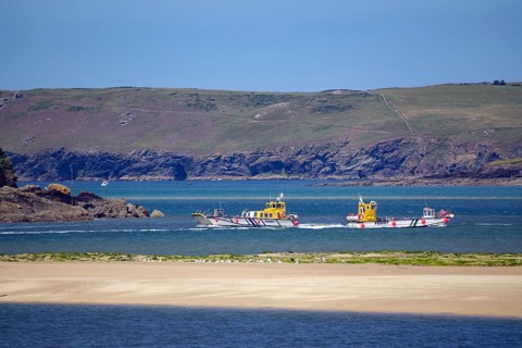 Two small passagi in blue water against a rocky coastline and green cliffs, Camel Trail, Padstow,