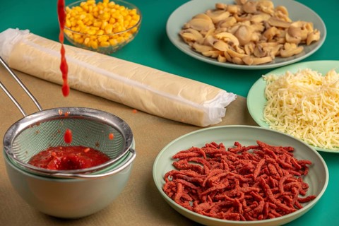 Tomato sauce drips into a sieve alongside other ingredients for pizza