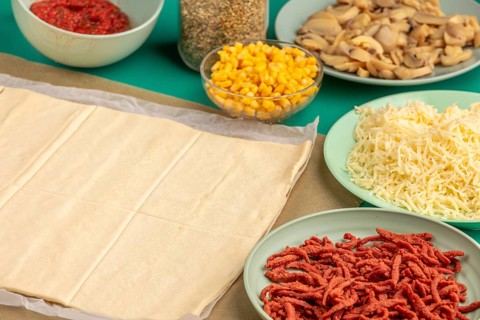 Pizza, dough on baking paper with prepared ingredients in trays