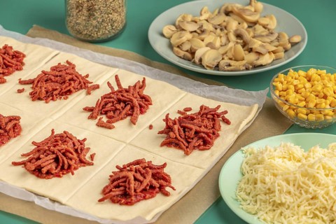 Sliced dough squares with tomato paste and bacon alongside other ingredients for pizza, balls
