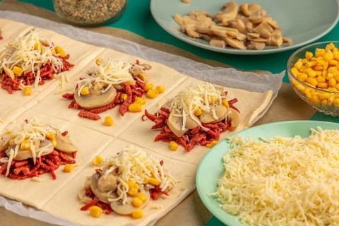 Sliced dough squares with tomato paste, bacon, mushrooms, sweetcorn and cheese alongside other