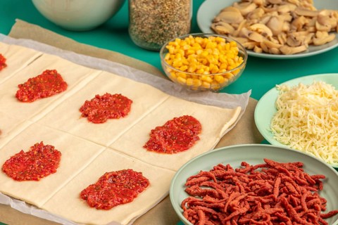 Cut pastry squares with tomato paste and prepared ingredients