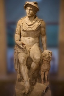Ancient marble sculpture of a seated man next to a ram, Hermes, seated, on display in the museum,