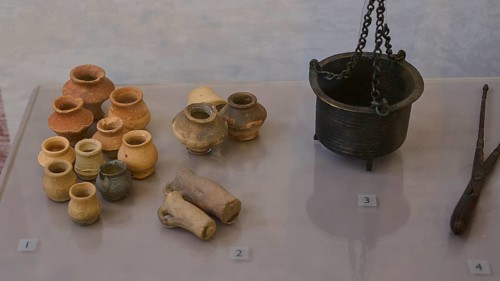 Collection of ancient ceramic artefacts, various pots and a metal crucible on display,