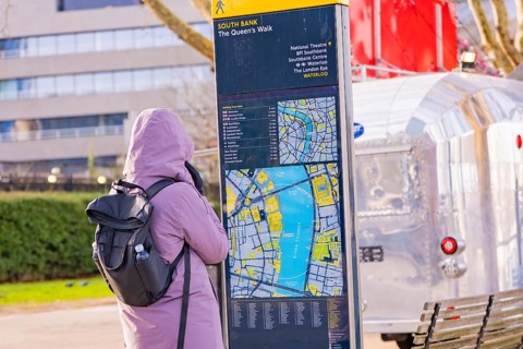 Woman wearing warm clothes looking at a map at a city map kiosk, London, United Kingdom, World