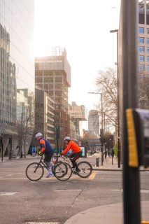 Two cyclists ride on an urban road, sunlight reflected on the buildings, London, United Kingdom,