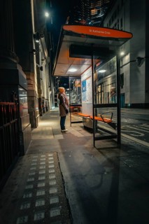 Person waiting at an illuminated bus stop in a quiet city street at night, London, United Kingdom,