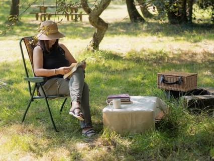 Woman enjoying a peaceful afternoon reading a book in a folding chair under a tree