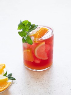 Glass of cold fruit juice with orange, lemon, and mint on a white background