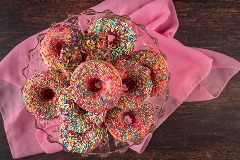Donuts with colorful sprinkles on glass plate and pink fabric on wooden table