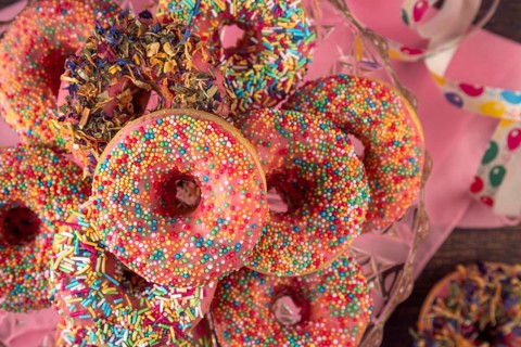 Colourful donuts with sprinkles and streamers on pink cloth, carnival