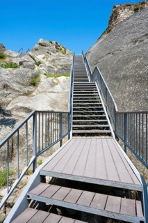 Metal staircase leads up between rocky walls under blue sky, Uplistsikhe cave town, Uplistsikhe,