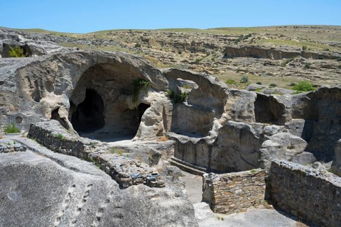 Rock formations with caves and ruins in a vast landscape under blue sky, Uplistsikhe cave town,