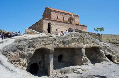 Historic church on a rock with caves and tourists on a clear day, 10th century princely church,
