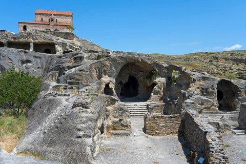 Ancient cave with entrances, dominated by an old building and surrounded by nature, 10th century