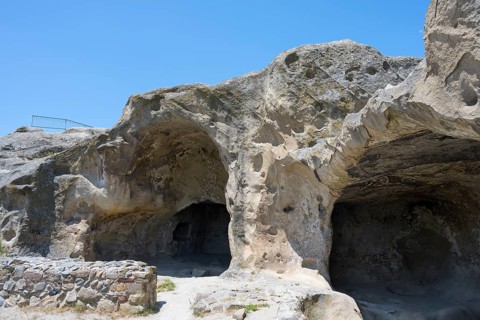 Rock formation with cave entrances under blue sky in natural landscape, Uplistsikhe cave town,
