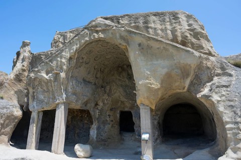 Ancient cave architecture with stone entrances and a clear sky, cave opening with gable fragment,