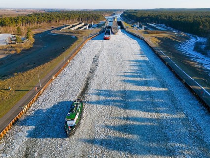 A ship sails through a long, icy waterway lined with locks in a wide landscape, aerial view,