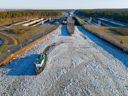 A lock channel with moving ships, frozen in a winter environment with forests, aerial view,