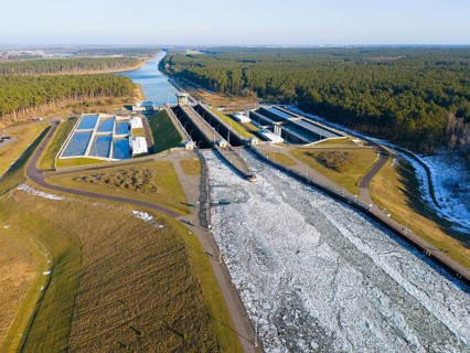 Drone view of a canal in winter with ice, snow-covered soil and adjacent forest, aerial view,