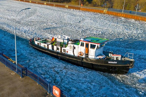 A ship navigates through an ice-covered channel in the harbor area in cold winter weather, aerial