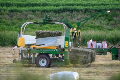 Tractor wraps hay bales in a field with a round baler in plastic film to preserve hay, Osnabrücker