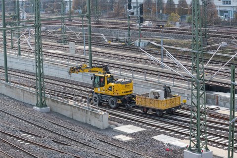 Yellow excavator next to railroad tracks on a large construction site in an urban environment,