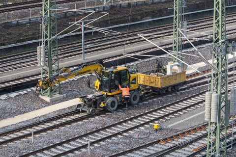 A construction site scene with yellow excavator and wagon near railroad tracks, Untertürkheim