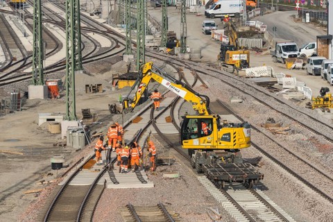 Rail construction with a group of workers and a yellow construction machine vehicle on the