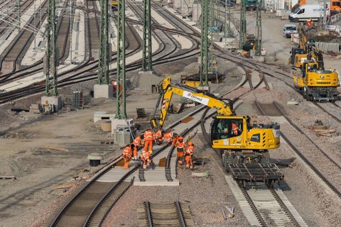 Workers wearing orange safety clothing work on railroad tracks with technical equipment,