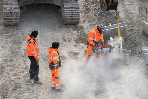 Construction workers in protective clothing work with machines on a dusty construction site,