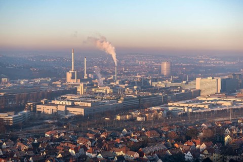Aerial view of a city at dusk, with industrial structures and suburban houses, sky and smoke