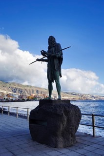 Bronze statue of a man with spear on the coast against blue sky and clouds, Candelaria Tenerife