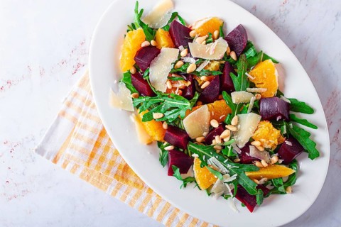 A salad made with chunks of beet, orange slices, and arugula. It is topped with cheese shavings and