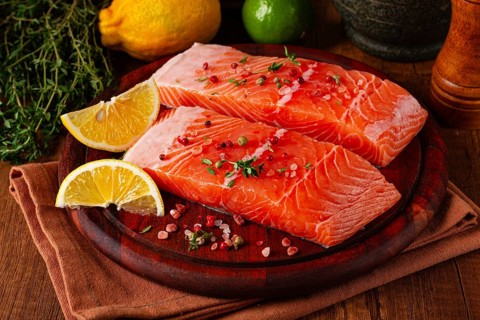 Two salmon fillets rest on a wooden platter. The fillets are garnished with herbs and spices. Lemon