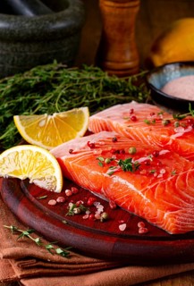 Two salmon fillets rest on a wooden platter. The fillets are garnished with herbs and spices. Lemon