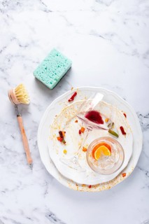 Dishes are stacked on a kitchen counter with food remnants after a meal. A cleaning brush and