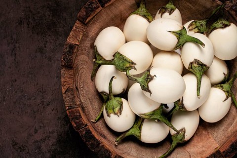 White mini eggplant, in a wooden bowl, on the table, close-up