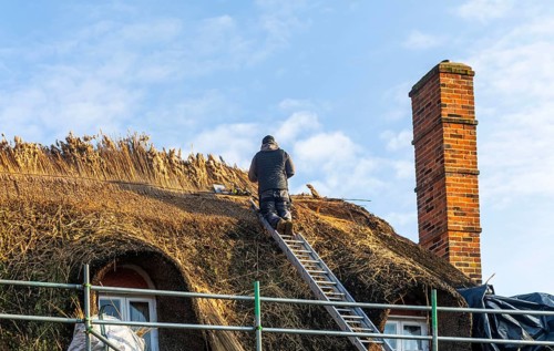 Thatcher at work replacing thatch ridge of thatched country pub building, Sorrel Horse, Shottisham,