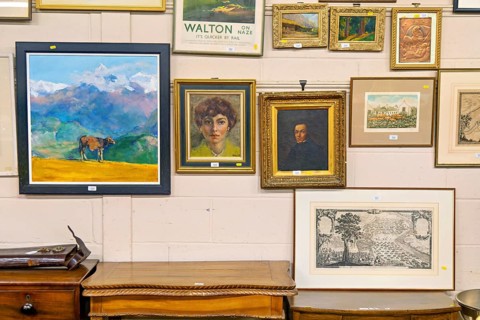 Various lots of pictures and paintings hanging on wall at auction house, UK