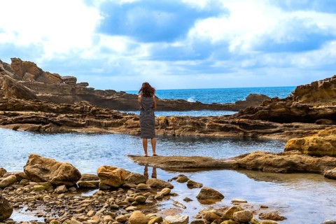 Woman standing on a natural rock formation, looking out at the rugged jaizkibel coast and atlantic