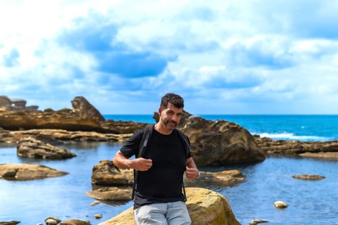Man with a beard and backpack standing on coastal rocks by the sea, exploring the unique geological