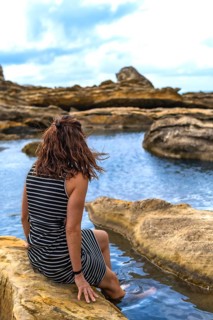Woman sitting on coastal rock formations, enjoying the calm water and rugged landscape of