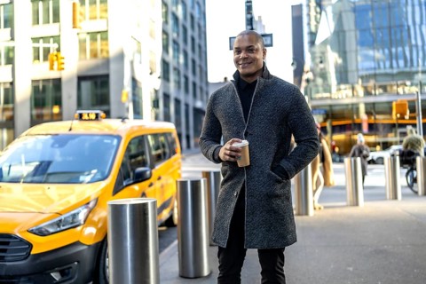 Businessman standing on a new york city street with a coffee cup, a yellow taxi passing in the