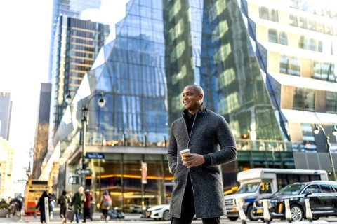 Happy business professional standing on a busy manhattan street, holding a takeaway coffee cup,