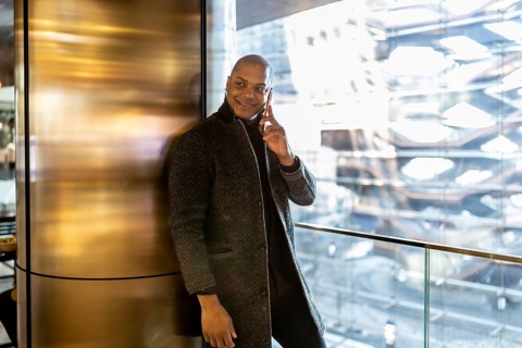 Black businessman standing in a modern building with city views, engaged in a phone call and