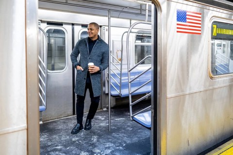 Young businessman standing on a subway car with a coffee cup, looking out through the open door,