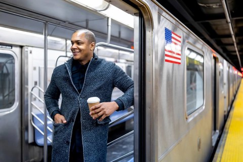 Young businessman boarding a new york city subway, smiling with a takeaway coffee as he steps onto