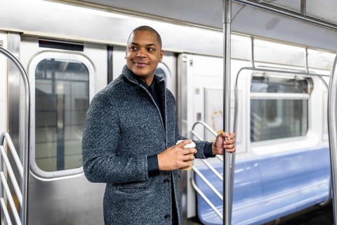 Young businessman traveling by public transport in manhattan, holding a coffee cup and looking
