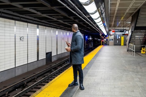Businessman in a winter coat stands on the yellow safety strip of a subway platform, holding a